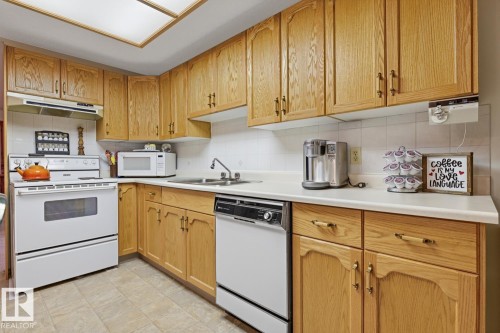 The kitchen features extensive wood cabinetry, white countertops, a white tile backsplash, and a white oven with an overhead range hood - 16108 100 Street, Edmonton, AB - Indoor Photo Showing Kitchen With Double Sink