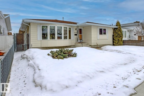 The property features a light-colored exterior, a bay window with decorative window coverings, and a front yard with a low-lying shrub - 16108 100 Street, Edmonton, AB - Outdoor