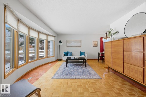 Living area featuring parquet wood flooring, a curved bay window with blinds, and white walls - 16108 100 Street, Edmonton, AB - Indoor
