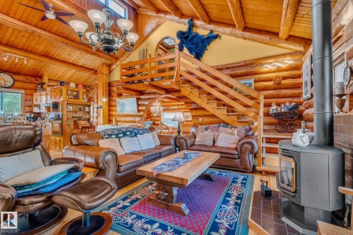 Spacious living room featuring log walls, a wood-burning stove, a wooden staircase, and a vaulted ceiling with exposed beams - 60017 Range Road 42, Rural Barrhead County, AB - Indoor Photo Showing Other Room