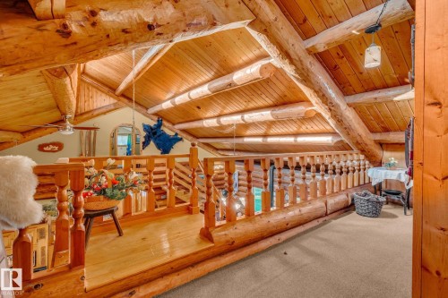Loft area featuring exposed log beams, wooden ceilings, a wooden railing, and carpeted flooring - 60017 Range Road 42, Rural Barrhead County, AB - Indoor
