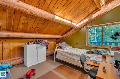 This room features an exposed beam ceiling with wood paneling, a large window offering natural light and views of foliage, and a neutral-toned carpet - 60017 Range Road 42, Rural Barrhead County, AB - Indoor