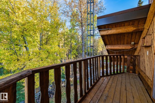 The property features a wooden balcony with a rustic railing, overlooking a vibrant treeline with lush foliage - 60017 Range Road 42, Rural Barrhead County, AB - Outdoor With Exterior