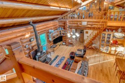 Expansive open-concept living space featuring natural wood log walls, high ceilings with exposed wood beams, and warm wood flooring - 
