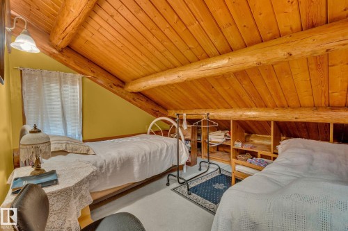 This room features warm wood paneling and exposed wooden beams on the sloped ceiling, creating a distinctive architectural style - 60017 Range Road 42, Rural Barrhead County, AB - Indoor Photo Showing Bedroom