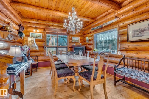 The property features a dining area with exposed log walls and ceiling, a chandelier light fixture, and hardwood floors - 60017 Range Road 42, Rural Barrhead County, AB - Indoor Photo Showing Dining Room With Fireplace