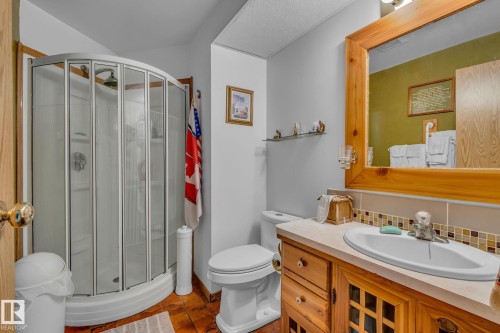This bathroom features a shower enclosure with curved glass doors, a vanity with a light wood finish and a white sink, and a framed mirror - 60017 Range Road 42, Rural Barrhead County, AB - Indoor Photo Showing Bathroom
