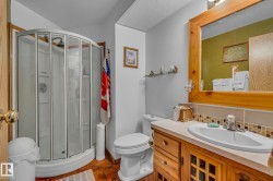 This bathroom features a shower enclosure with curved glass doors, a vanity with a light wood finish and a white sink, and a framed mirror - 