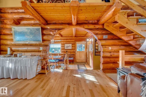 The property features a spacious room with light hardwood floors, log walls and ceiling, and an arched wooden entryway - 60017 Range Road 42, Rural Barrhead County, AB - Indoor