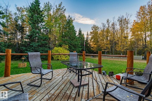 The property features a spacious outdoor wooden deck with a log railing, overlooking a large grassy area and mature trees - 60017 Range Road 42, Rural Barrhead County, AB - Outdoor With Deck Patio Veranda