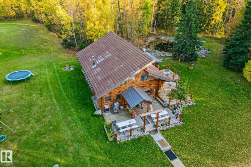 Aerial view of the property featuring a log cabin style home with a brown roof, an extensive lawn, and surrounding trees - 60017 Range Road 42, Rural Barrhead County, AB - Outdoor