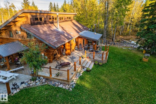 The property features a log cabin style exterior with a large wooden deck and a lush green lawn - 60017 Range Road 42, Rural Barrhead County, AB - Outdoor With Deck Patio Veranda