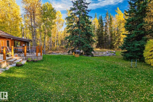 The property features a spacious yard with a lush lawn, surrounded by dense trees, including both deciduous and evergreen varieties - 60017 Range Road 42, Rural Barrhead County, AB - Outdoor With Deck Patio Veranda