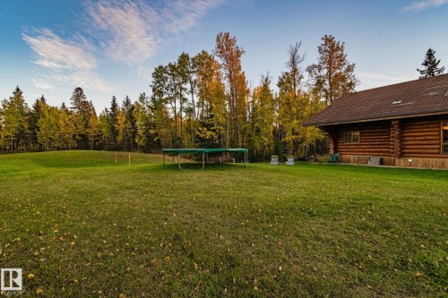 The property features an extensive lawn area, mature trees, and a log cabin style exterior with a brown roof - 60017 Range Road 42, Rural Barrhead County, AB - Outdoor