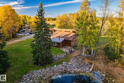 The property features a wood-sided building with a metal roof, surrounded by mature trees with vibrant autumn foliage - 60017 Range Road 42, Rural Barrhead County, AB - Outdoor With View