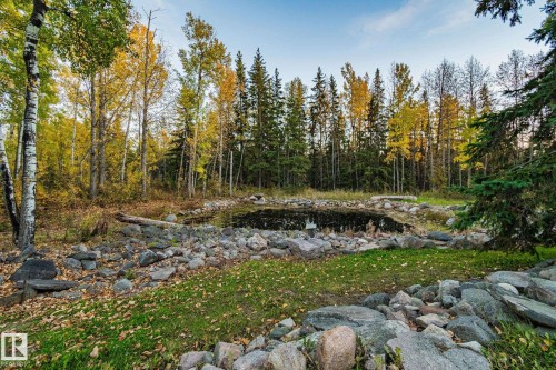 The property features a serene pond surrounded by natural rock landscaping and mature trees - 60017 Range Road 42, Rural Barrhead County, AB - Outdoor