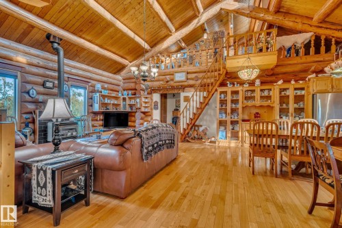 The spacious living area features hardwood floors, exposed log walls, and a wood-burning stove - 60017 Range Road 42, Rural Barrhead County, AB - Indoor