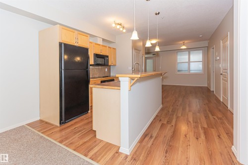 This open concept living space features a kitchen with black appliances, light wood cabinetry, and a peninsula with pendant lighting - 415 10503 98 Avenue, Edmonton, AB - Indoor Photo Showing Kitchen