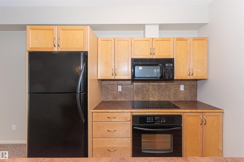 The kitchen features light wood cabinetry, a black refrigerator, a built-in oven, and a microwave - 415 10503 98 Avenue, Edmonton, AB - Indoor Photo Showing Kitchen