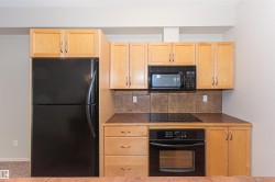 The kitchen features light wood cabinetry, a black refrigerator, a built-in oven, and a microwave - 