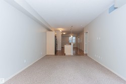 Open-concept living space featuring neutral-toned carpet, light-colored walls, and a view towards the kitchen with hardwood flooring - 