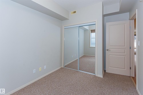 The room features a neutral color palette, carpet flooring, and a closet with mirrored sliding doors - 415 10503 98 Avenue, Edmonton, AB - Indoor Photo Showing Other Room