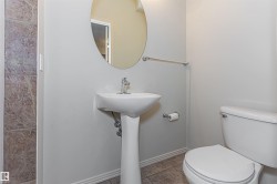 Bathroom featuring a pedestal sink with a chrome faucet, a white toilet, and a circular mirror - 