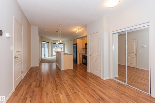 Open concept living area with hardwood flooring, a kitchen featuring pendant lighting and black appliances, and a mirrored closet - 415 10503 98 Avenue, Edmonton, AB - Indoor Photo Showing Other Room