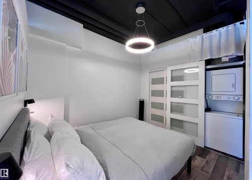 The room features a contemporary ceiling light fixture, a split-system air conditioning unit, and a set of white sliding closet doors with frosted glass panels - 1701 10024 Jasper Avenue, Edmonton, AB - Indoor Photo Showing Bedroom