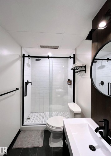 Bathroom featuring a walk-in shower with subway tile walls and a hexagonal tiled floor, a vanity with an integrated sink, and a round mirror with a black frame - 1701 10024 Jasper Avenue, Edmonton, AB - Indoor Photo Showing Bathroom