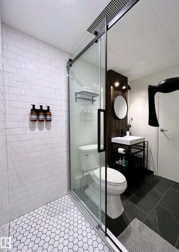 Bathroom featuring a walk-in shower with white subway tile walls and a hexagonal tile floor, a glass shower door with a black frame, and a white toilet - 1701 10024 Jasper Avenue, Edmonton, AB - Indoor Photo Showing Bathroom