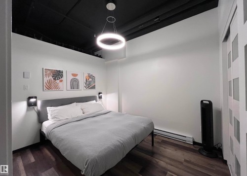 This room features dark wood-style flooring, a light-colored headboard, and a modern circular light fixture - 1701 10024 Jasper Avenue, Edmonton, AB - Indoor Photo Showing Bedroom
