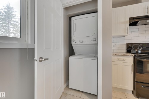 Laundry area featuring a stacked washer and dryer, adjacent to a kitchen with white cabinetry, a tiled backsplash, and a black range - 13211 104 Street, Edmonton, AB - Indoor Photo Showing Laundry Room