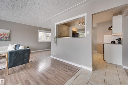 This living area features hardwood style flooring, neutral wall colors, and a window providing natural light - 13211 104 Street, Edmonton, AB - Indoor