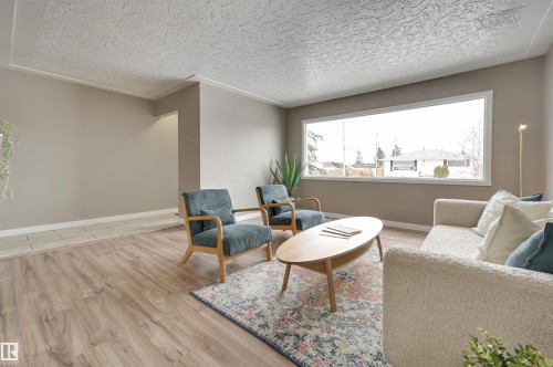 Living area featuring hardwood flooring, a large window providing natural light, and a textured ceiling - 13211 104 Street, Edmonton, AB - Indoor Photo Showing Living Room