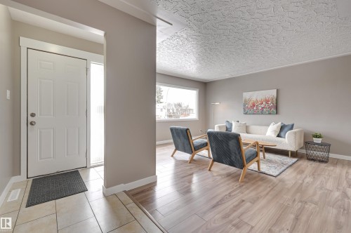 Inviting entry with tile flooring and a side light, leading into a living area featuring wood-look flooring and a large window - 13211 104 Street, Edmonton, AB - Indoor
