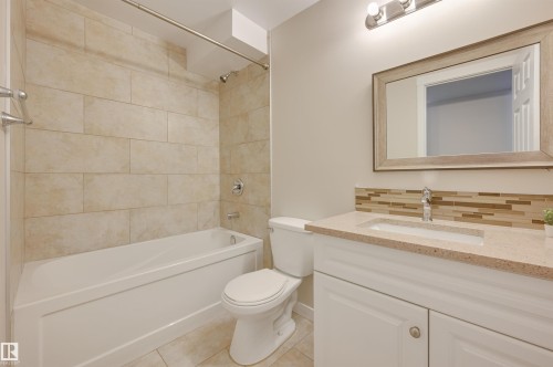 Bathroom featuring a white bathtub with tiled surround, a white vanity with a light-colored countertop, and a decorative mirror - 13211 104 Street, Edmonton, AB - Indoor Photo Showing Bathroom
