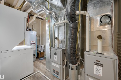 The property features a utility area with a water heater, furnace, and laundry machines, all situated on a wood-look floor - 13211 104 Street, Edmonton, AB - Indoor Photo Showing Basement