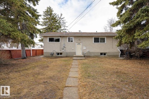 The property features a stucco exterior, a fenced yard, and mature evergreen trees - 13211 104 Street, Edmonton, AB - Outdoor