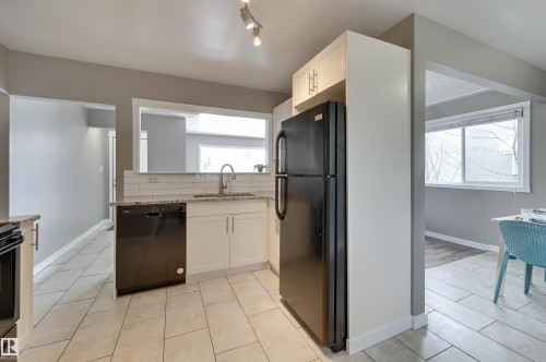 The kitchen features tiled flooring, white cabinetry, a dishwasher, a refrigerator, and a window - 13211 104 Street, Edmonton, AB - Indoor Photo Showing Kitchen