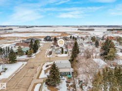 Aerial view of the property and its surrounding neighborhood, featuring residential homes, mature trees, and open fields under a clear sky - 