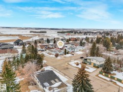 Aerial view of the property and surrounding neighborhood, featuring residential homes, mature trees, and open fields under a bright sky - 
