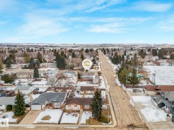 Aerial view of the property and its surrounding neighborhood, featuring a paved road, scattered trees, and residential homes - 