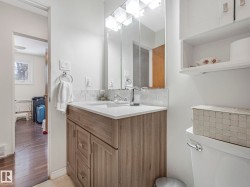 The bathroom features a vanity with a light wood-grain finish, a white countertop, and a chrome faucet - 