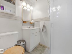 The bathroom features a vanity with a white cabinet and countertop, a toilet with a wooden seat, and a shower enclosure - 
