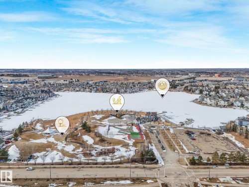 Aerial view showcasing a large frozen lake surrounded by residential properties, with a visible road in the foreground and a distant cityscape under a blue sky - 8112 Summerside Grande Boulevard, Edmonton, AB - Outdoor With View