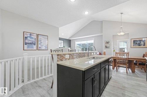 The kitchen features an island with a light-colored countertop and a tile backsplash, with a dining area visible beyond - 8112 Summerside Grande Boulevard, Edmonton, AB - Indoor