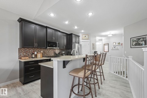 Kitchen with dark cabinetry, light countertops, and a patterned backsplash - 8112 Summerside Grande Boulevard, Edmonton, AB - Indoor Photo Showing Kitchen With Upgraded Kitchen