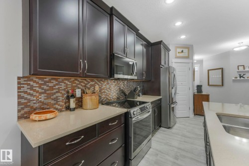 The kitchen features dark wood cabinetry, light-colored countertops, a tile backsplash with a mosaic pattern, and stainless steel appliances - 8112 Summerside Grande Boulevard, Edmonton, AB - Indoor Photo Showing Kitchen With Upgraded Kitchen