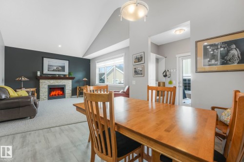 The living space features a stone-clad fireplace with a mantel, vaulted ceilings, and a window with blinds - 8112 Summerside Grande Boulevard, Edmonton, AB - Indoor Photo Showing Dining Room With Fireplace